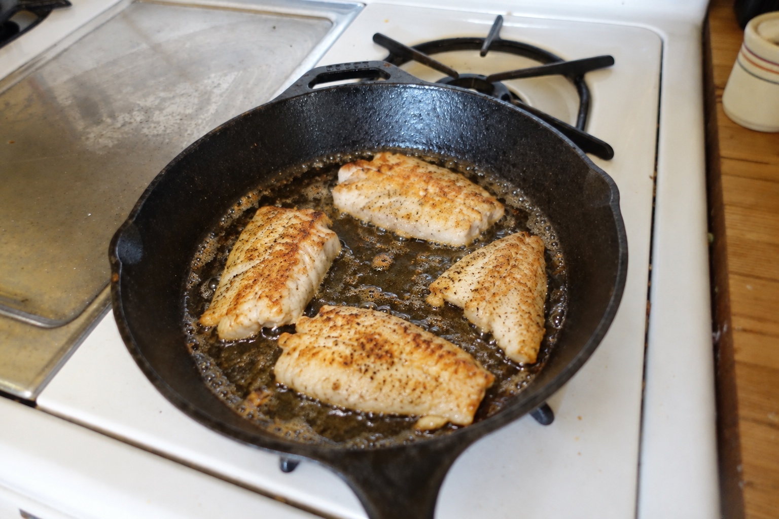Fish fillets frying in shallow oil in a skillet on the stove